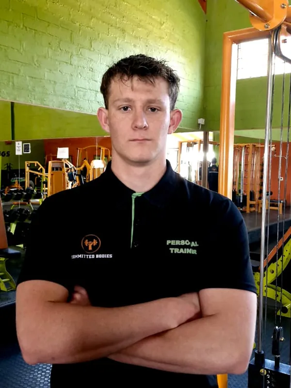 Jayson, arms folded, on the gym floor in front of the lime brick wall