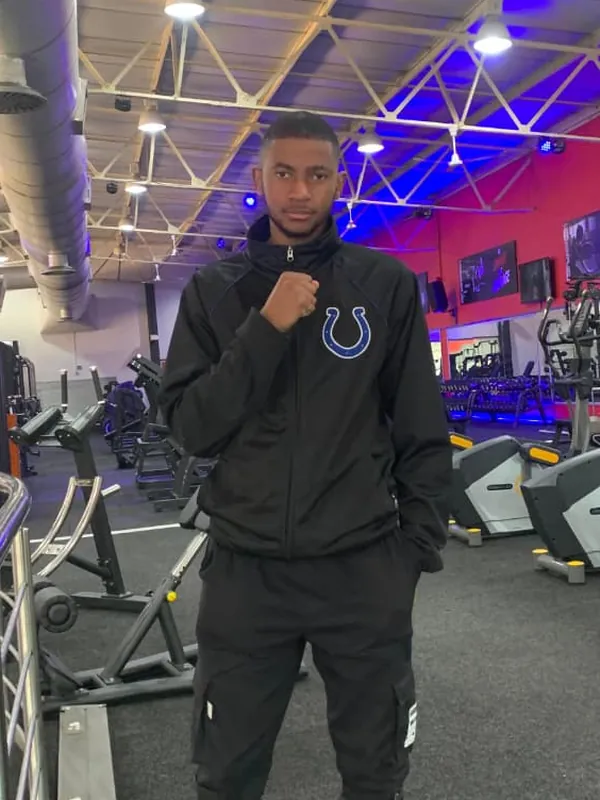 Kagitso in a black tracksuit, fist raised, on a gym floor